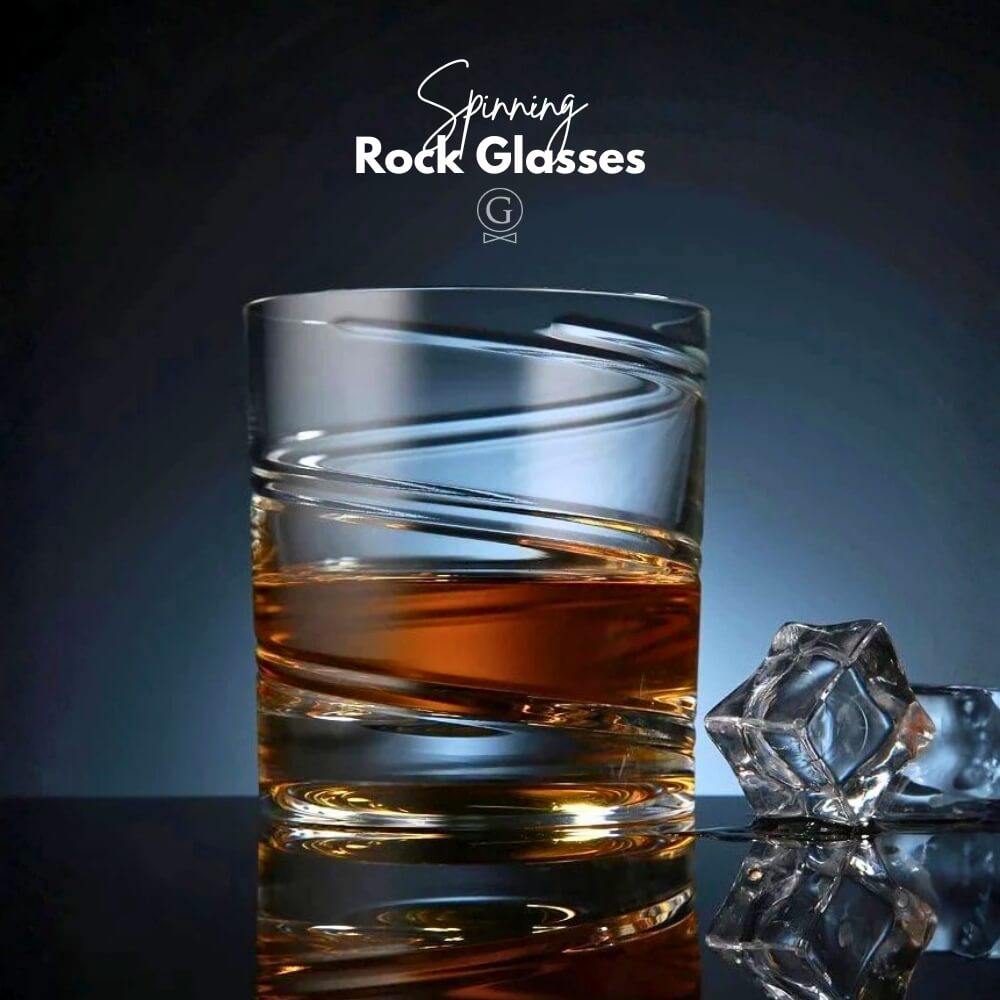 Glass of whiskey with a large ice cube on a reflective surface, branded 'Spinning Rock Glasses'.