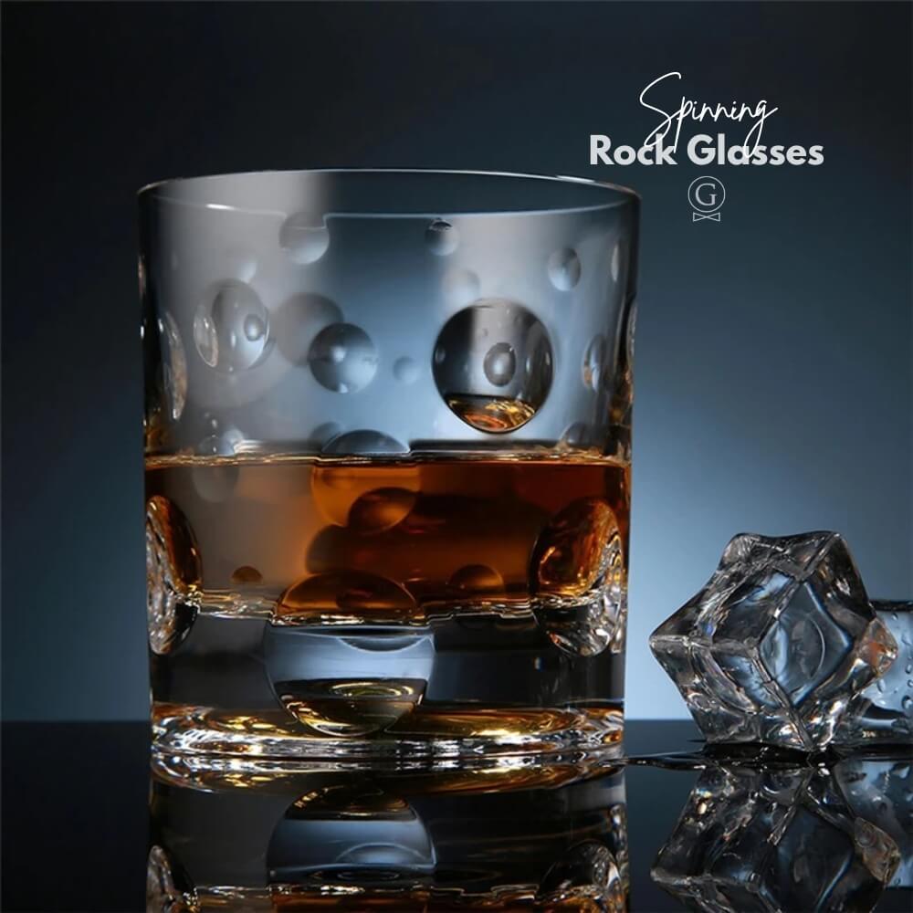 Glass of whiskey with ice cubes on a reflective surface, branded 'Sparrow Rock Glasses'.